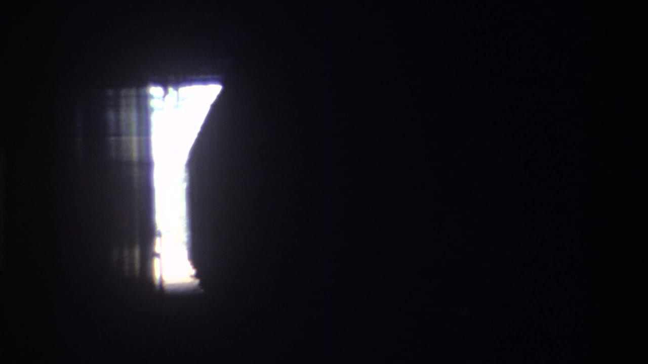 Dark transition frame from an 8mm home movie on a moving train, showing a bright window opening against a near-black interior, Hong Kong, 1982.