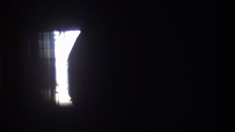 Dark transition frame from an 8mm home movie on a moving train, showing a bright window opening against a near-black interior, Hong Kong, 1982.