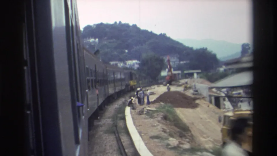 8mm footage of construction workers on a gravel embankment beside the Hong Kong railway, hillside buildings in background, c. 1982.