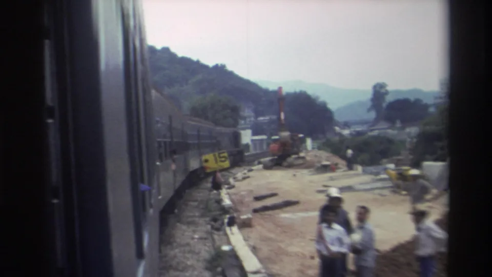 1982 Hong Kong — yellow trackside speed sign reading '15 Km/hr,' construction workers including one in a white hard hat, and an orange excavator visible alongside the railway.