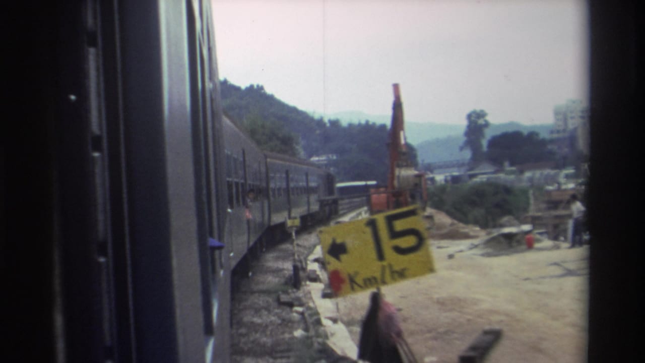 8mm footage, c.1982, Hong Kong — train passing construction site; yellow speed sign reading '15 Km/hr' and orange hydraulic excavator in background.