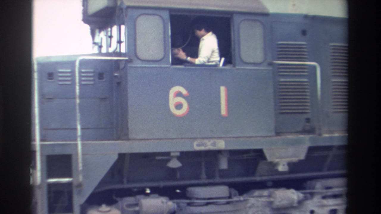 Close-up of blue-grey diesel locomotive number 61, conductor in white shirt visible in cab window.
