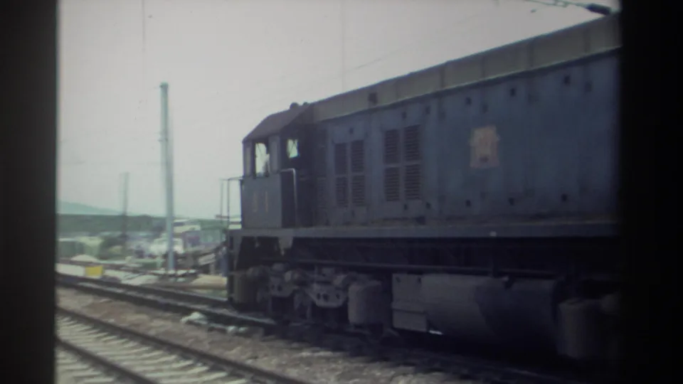 Rear section of diesel locomotive 61 moving away, railway tracks, utility poles and hazy industrial background, 1982 Taiwan, 8mm home movie.