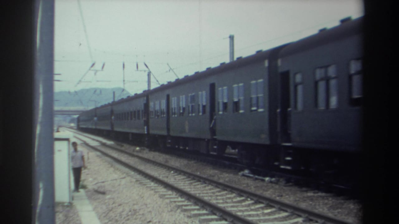 8mm footage from Taiwan, 1982, showing a multi-car electrified passenger train moving past a platform with a figure standing near the platform edge and hills visible in the distance.