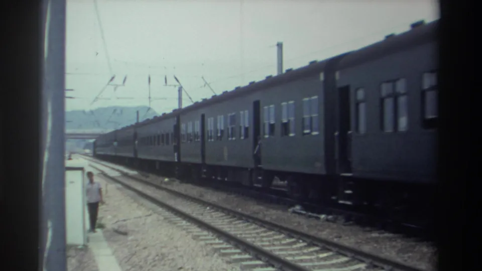 8mm footage from Taiwan, 1982, showing a multi-car electrified passenger train moving past a platform with a figure standing near the platform edge and hills visible in the distance.