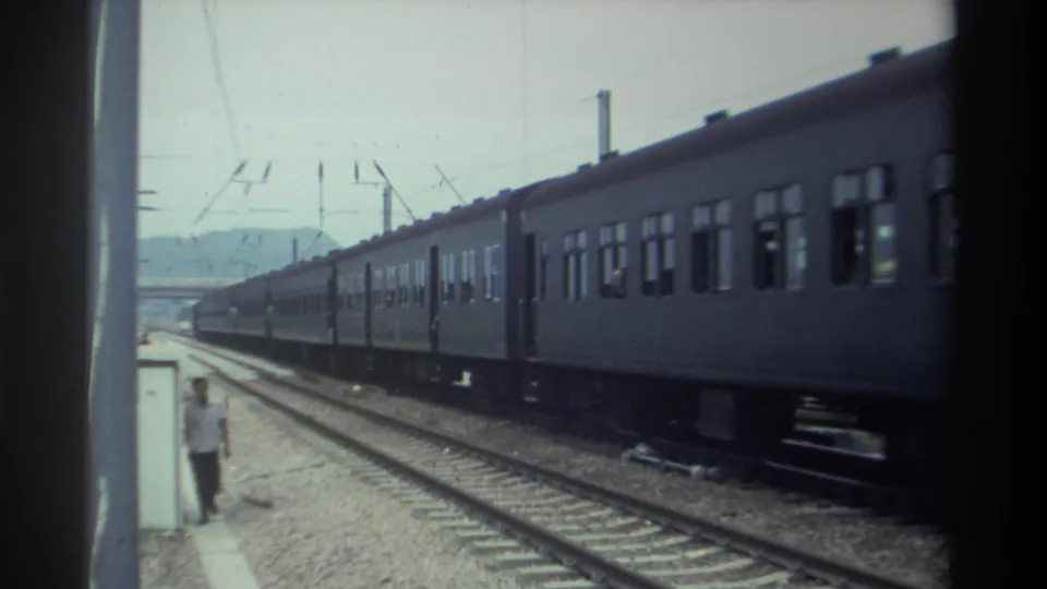 8mm home movie frame from Taiwan, 1982, with a long passenger train passing and a man walking along the platform edge, overhead catenary infrastructure clearly visible.