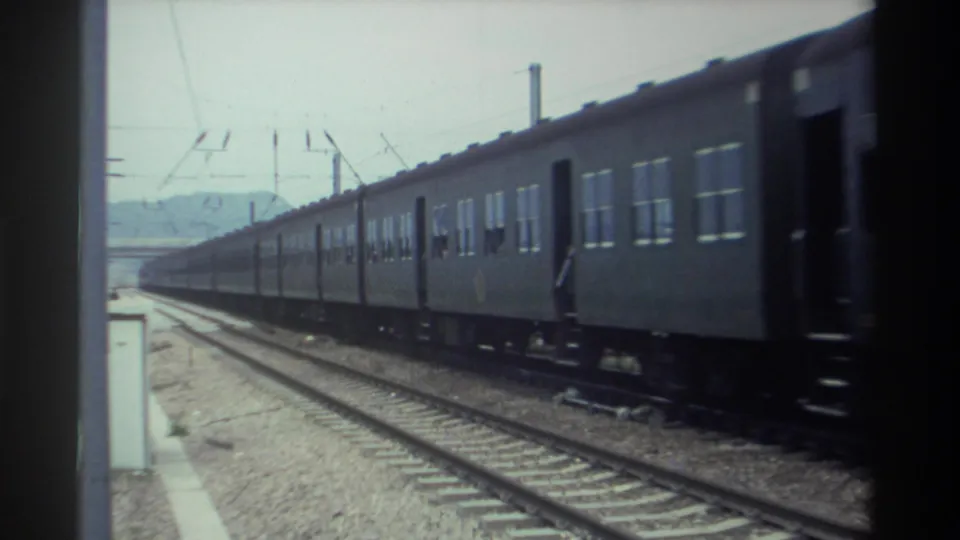 Passenger train passing a station platform in Taiwan, circa 1982, with parallel tracks, platform edge, and distant hills visible, 8mm film.