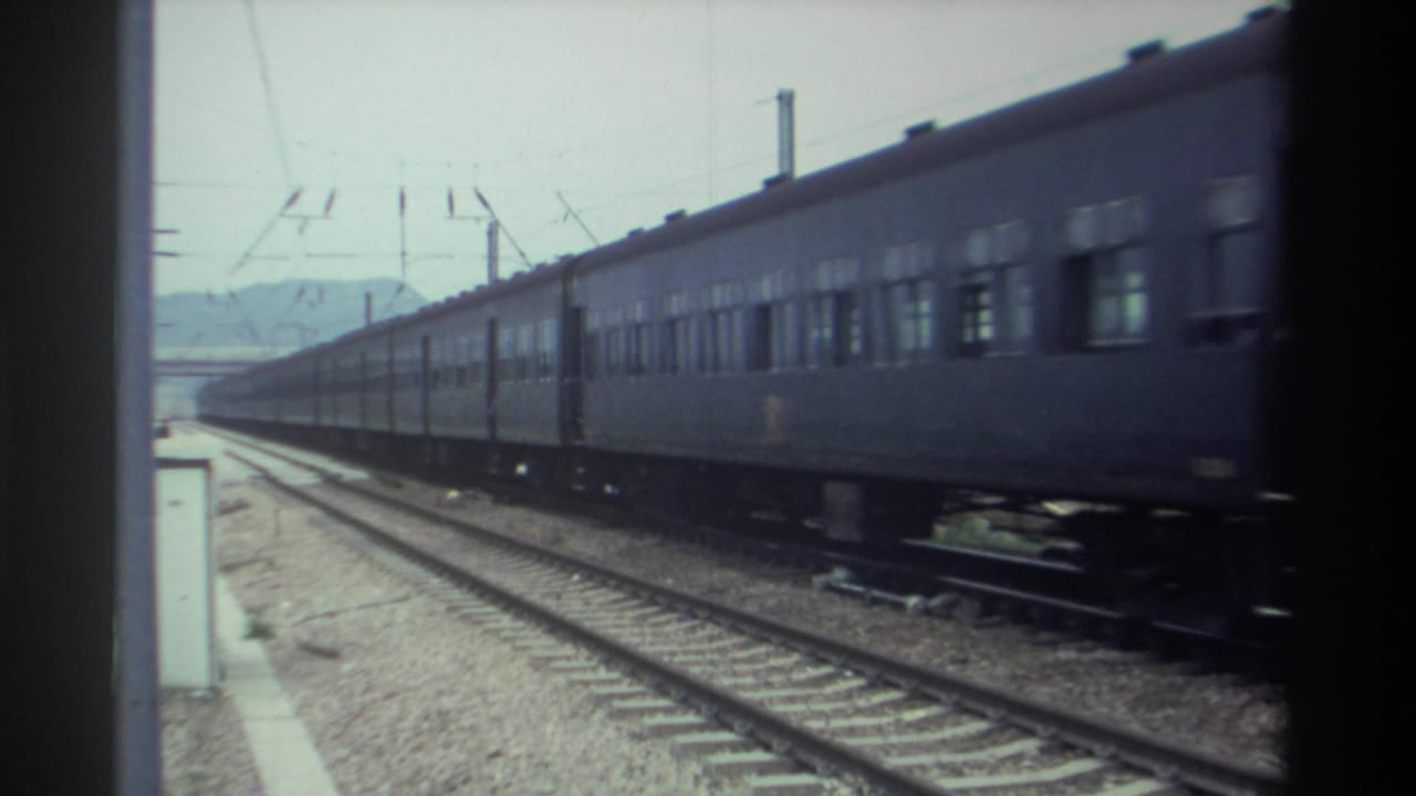 Dark-painted passenger train passing on electrified tracks in Taiwan, circa 1982, filmed on 8mm from a stationary trackside or platform position.