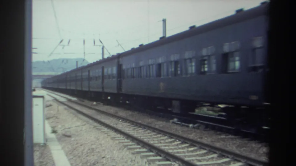 Dark-painted passenger train passing on electrified tracks in Taiwan, circa 1982, filmed on 8mm from a stationary trackside or platform position.