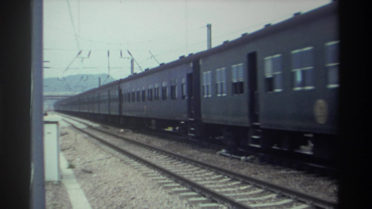 Dark-painted passenger train mid-pass on an electrified Taiwanese railway, circa 1982, filmed on 8mm with catenary infrastructure clearly overhead.