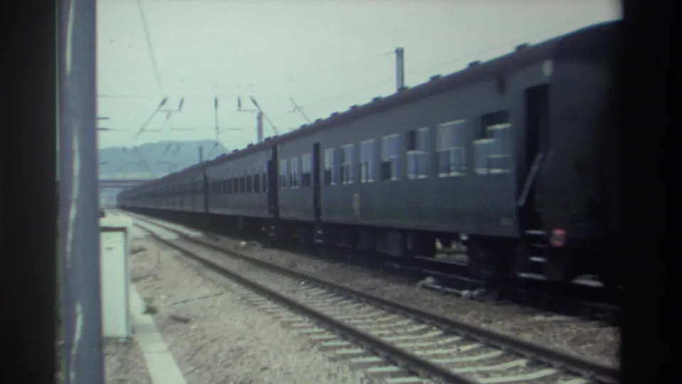 Rear section of a Taiwan passenger train nearing end of its pass, electrified rail infrastructure and distant hills visible, circa 1982 8mm footage.