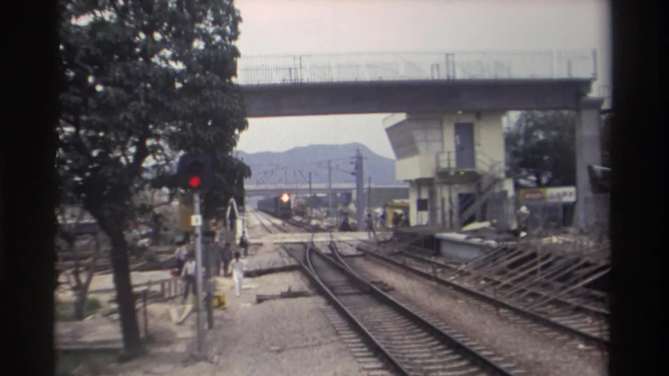 1982 Taiwan railway station; pedestrians move toward the boarding area as tracks converge beneath a concrete overpass and signal equipment.