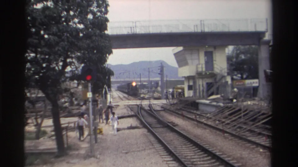 Taiwan railway station circa 1982; a train approaches on the right-hand track while pedestrians stand and walk near the platform area.