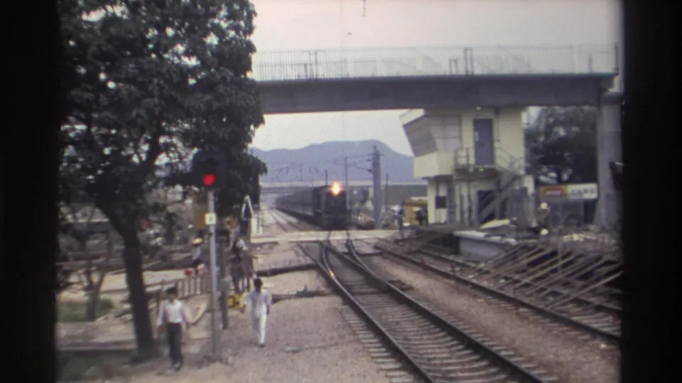 8mm film, Taiwan 1982: train with glowing headlight closing in on camera position; adults and a possible minor visible walking beside active tracks under concrete overpass.
