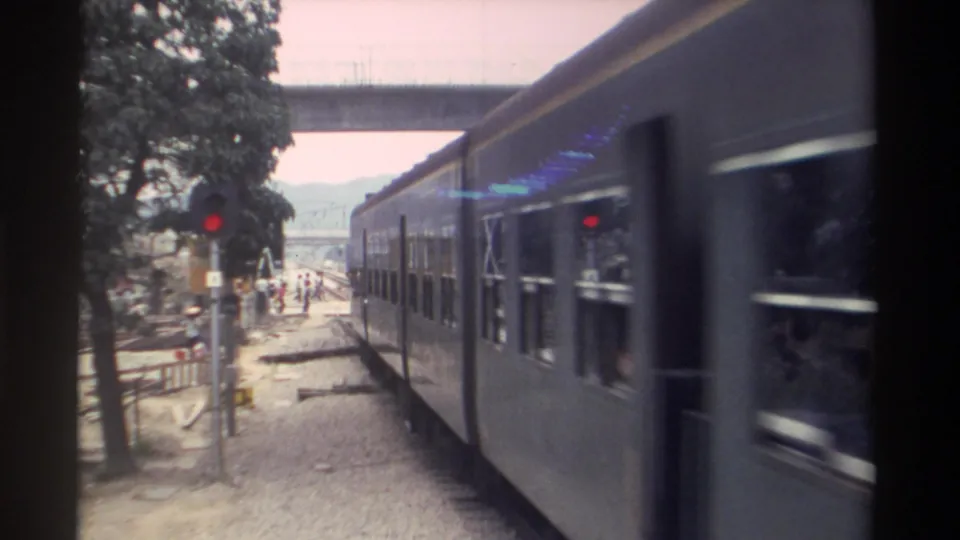 Mid-clip 8mm frame showing a Taiwan passenger train with red signals, a crossing marker, and pedestrians along the trackside, circa 1982.