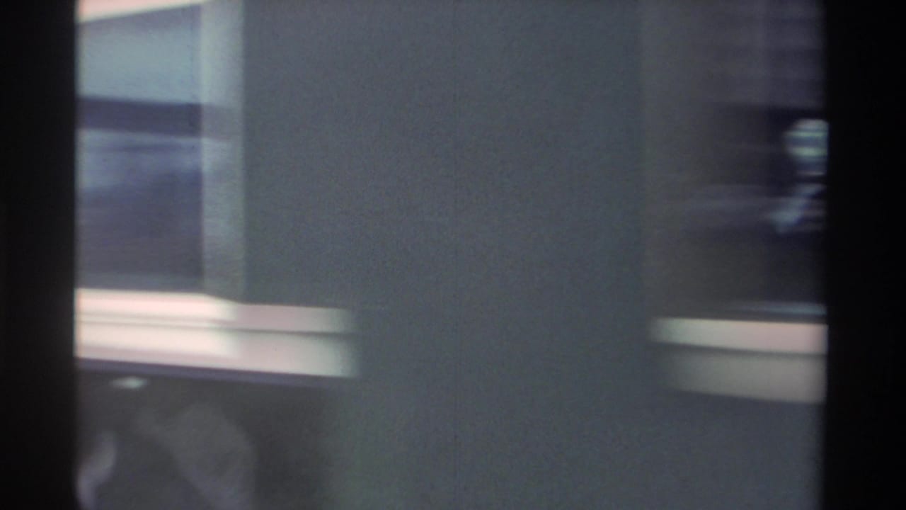 Motion-blurred close shot of a dark blue passenger train car with cream stripe, consistent with 1980s Taiwan Railways rolling stock, filmed on 8mm.