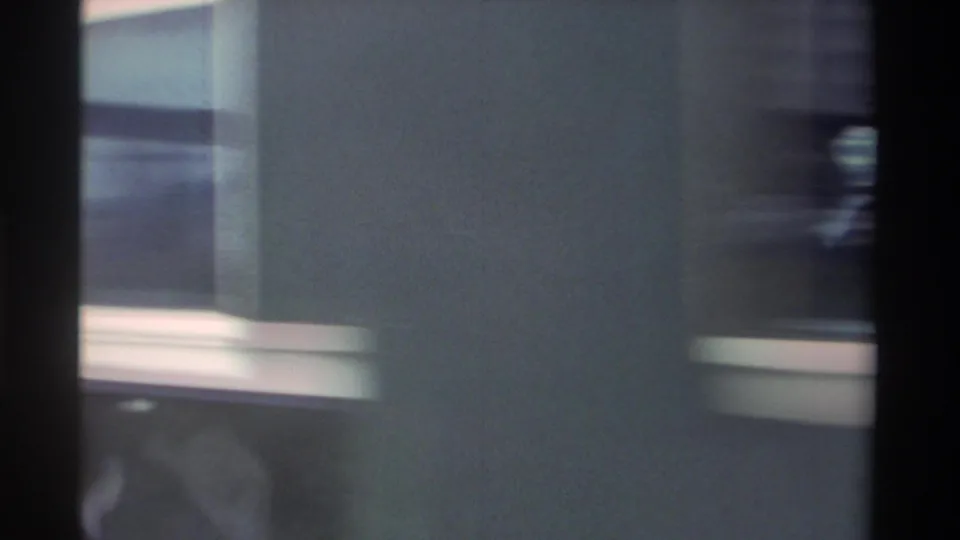 Motion-blurred close shot of a dark blue passenger train car with cream stripe, consistent with 1980s Taiwan Railways rolling stock, filmed on 8mm.