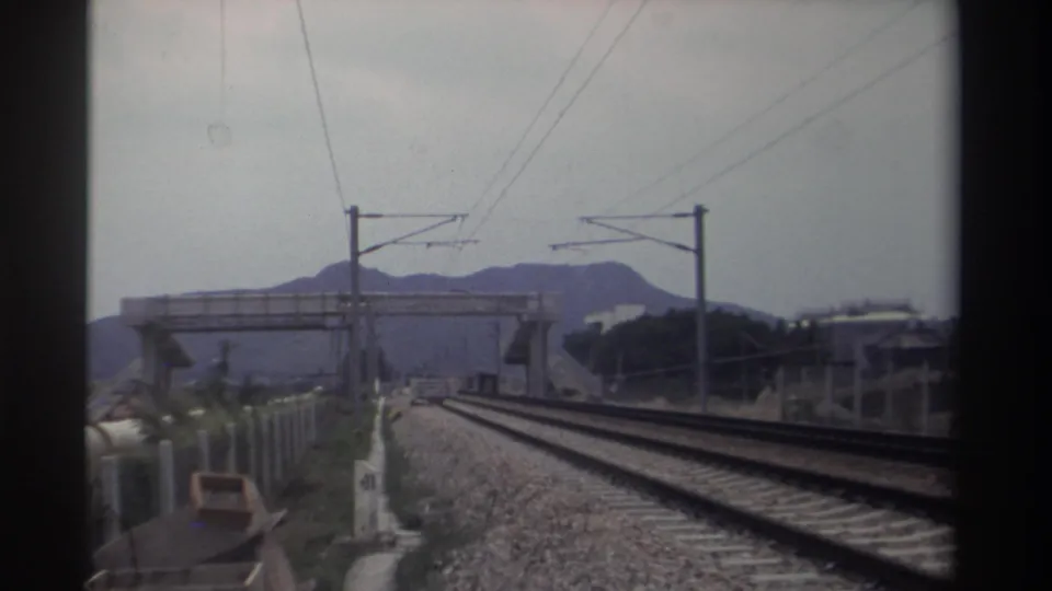 Forward-facing 8mm shot from a moving train showing electrified tracks, catenary wires, and mountain silhouettes in the distance, Taiwan, circa 1982.