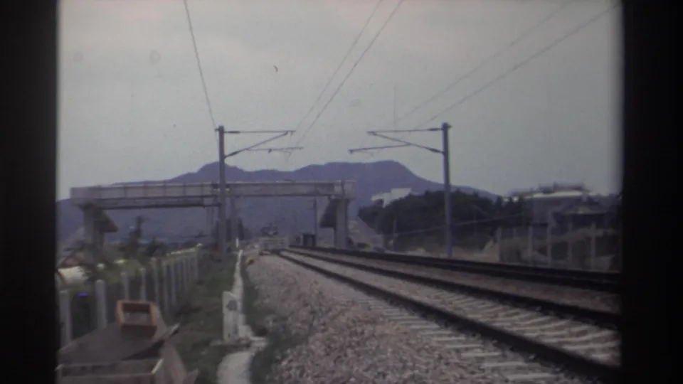 8mm view along electrified dual-track railway in Taiwan, 1982; catenary wire system and concrete overpass span the foreground tracks.