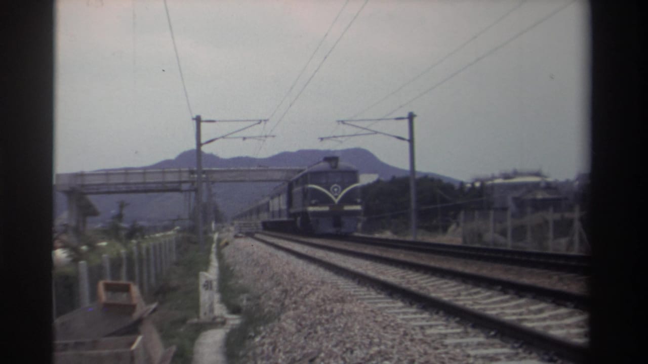 8mm footage of a locomotive advancing toward the camera on a Taiwan railway, circa 1982; overhead catenary system, white structures, and distant hills visible.