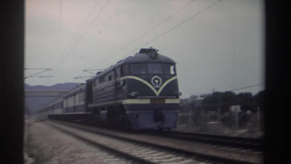Close 8mm frame of a locomotive cab front in Taiwan, circa 1982; white chevron markings and a circular institutional emblem clearly visible on the dark-painted nose.