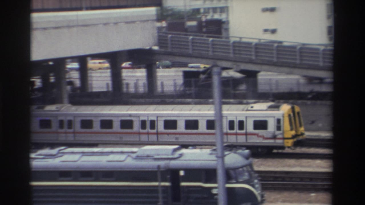 Silver and yellow commuter train beneath elevated concrete overpass, urban Taiwan circa 1982, 8mm home-movie footage.