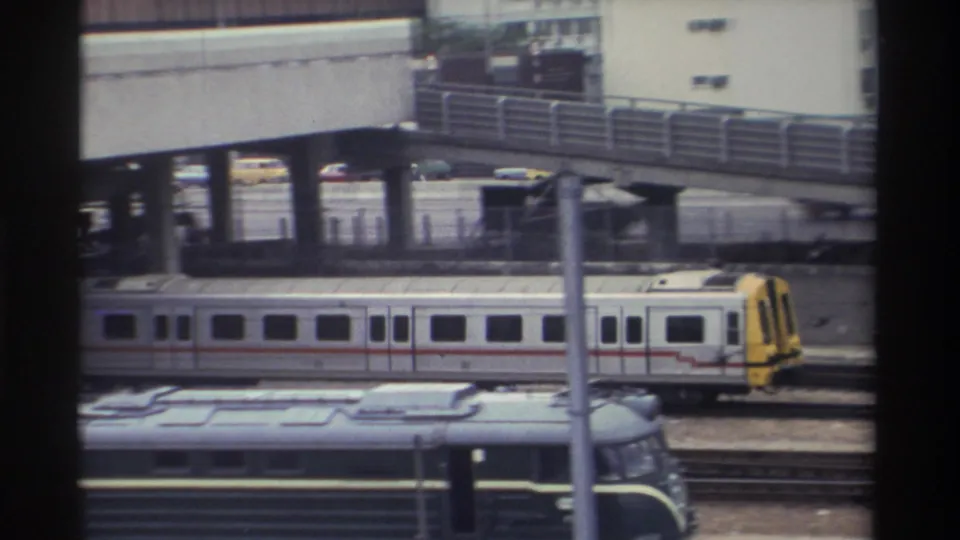 Silver and yellow commuter train beneath elevated concrete overpass, urban Taiwan circa 1982, 8mm home-movie footage.