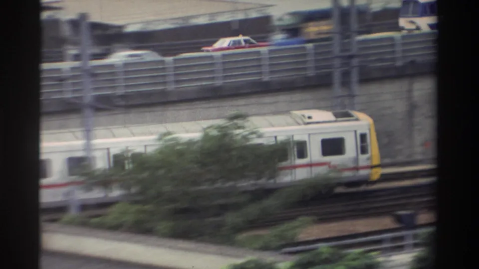 1982 Taiwan — commuter train with yellow rear cab moving along elevated tracks; road, cars, and trees visible in surrounding urban environment.
