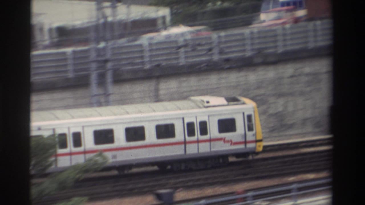 White passenger train with red stripe and yellow cab on elevated viaduct in Taiwan, 1982; highway traffic and catenary wires visible below through window frame.