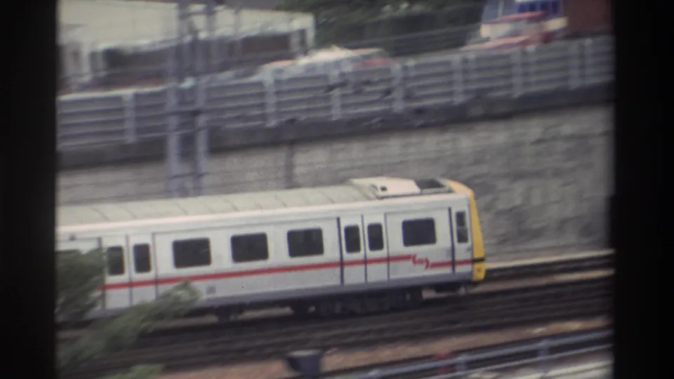 White passenger train with red stripe and yellow cab on elevated viaduct in Taiwan, 1982; highway traffic and catenary wires visible below through window frame.