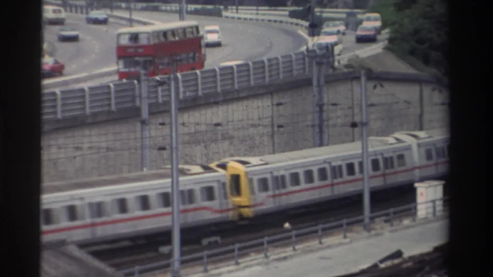 8mm home movie from Taiwan, c.1982: white and red passenger train passing below a curved highway where a red double-decker bus is visible.