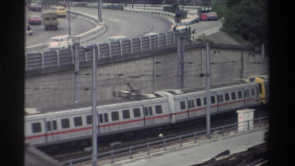 8mm frame from Taiwan, c.1982; train partially exits frame while road traffic and traffic signals remain visible on the curve above.