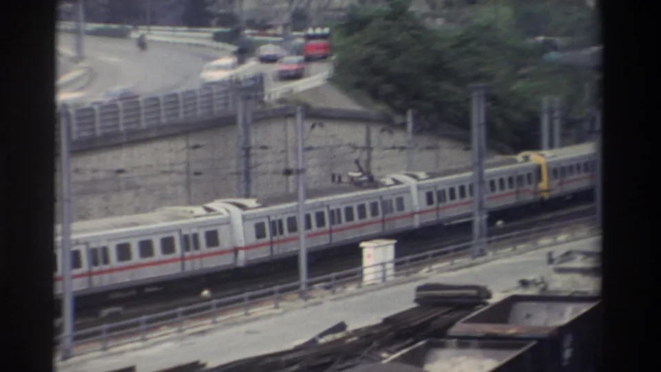 1982 Super 8 home movie from Taiwan: long passenger train with red horizontal stripe and yellow front car passing on elevated tracks beside a curved road.
