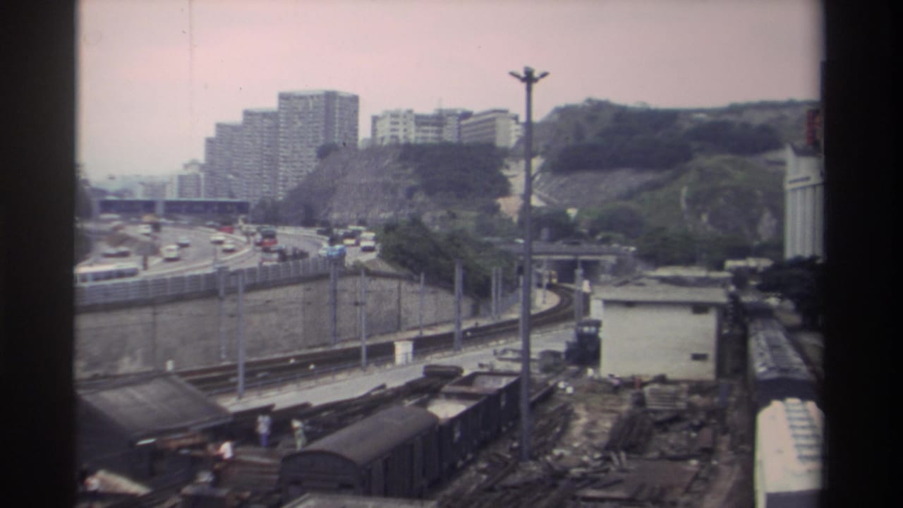 8mm film frame from Taiwan, circa 1982, capturing a rail yard, a curving elevated expressway with period vehicles, and densely built hillside housing estates.