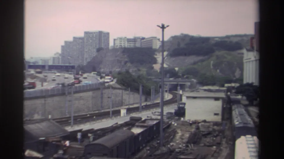 Super 8 frame from Taiwan, circa 1982, showing a sprawling freight yard, elevated urban expressway, and hillside residential towers representing the era's rapid urban growth.