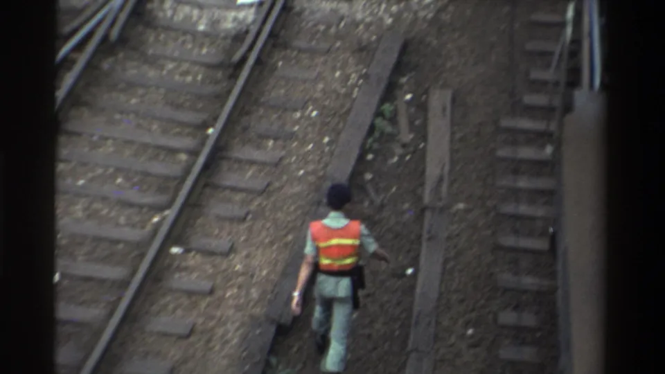 Railway worker in orange safety vest continues along Taiwan railway tracks away from camera, 8mm film circa 1982.