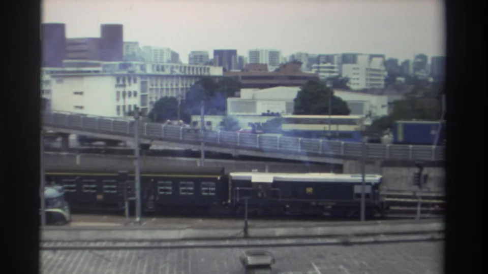 Final 8mm frame, Taiwan c. 1982 — trailing train cars below the elevated highway with a skyline of high-rise residential blocks visible through blue haze.