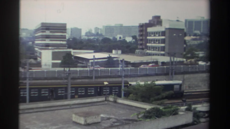 Final clip frame showing the elevated highway, mixed commercial and residential urban skyline, and foreground vegetation consistent with an early-1980s Taiwanese city district.