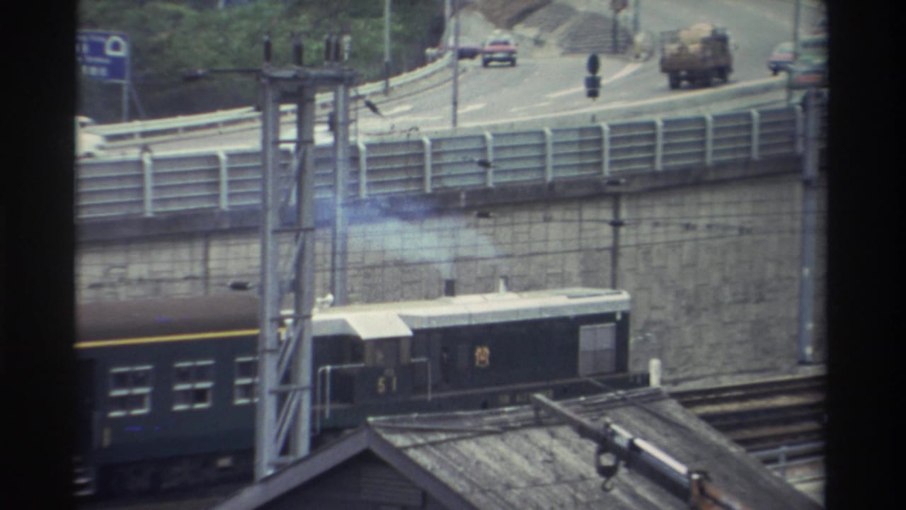 Dark green passenger train passing beneath a concrete highway overpass in Taiwan, 8mm home movie, c. 1982.