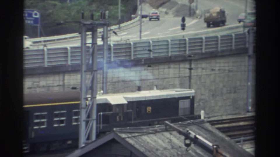 Dark green passenger train passing beneath a concrete highway overpass in Taiwan, 8mm home movie, c. 1982.