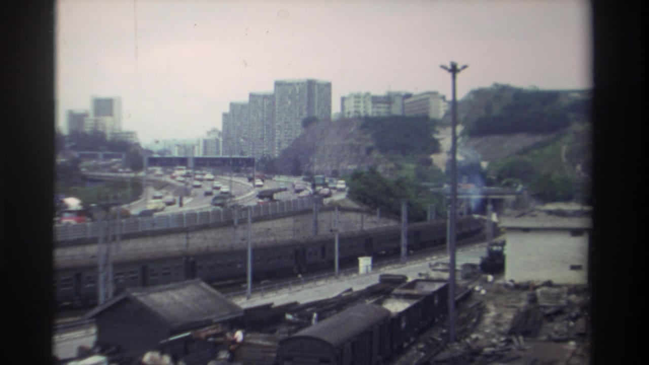 Wide view of a Taiwan transportation corridor, c. 1982 — train tracks, multi-lane expressway with traffic, and concrete apartment towers on a hillside, 8mm.
