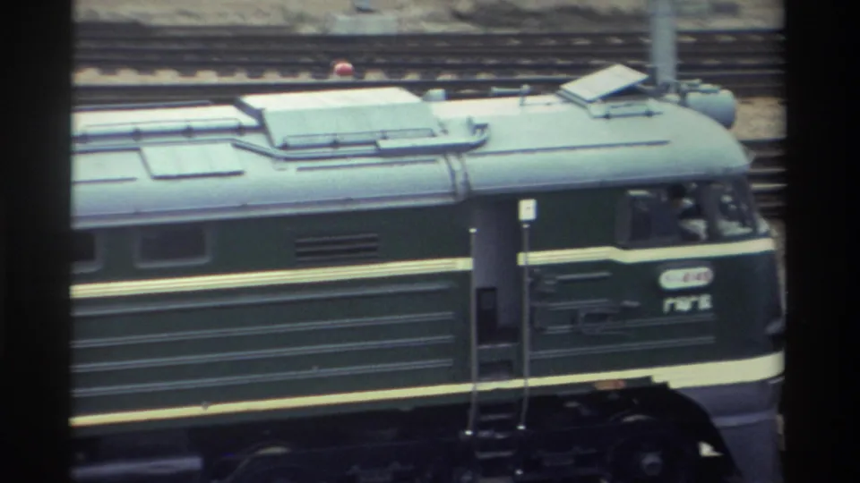 Side view of a dark green locomotive with yellow stripe and Chinese markings in a Taiwan rail yard, circa 1982; cab number plate and red marker light visible on the roof.
