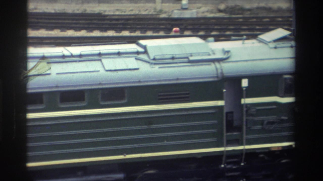 Close-up of a dark green passenger railway car at a platform, with tracks visible at the bottom of the frame.