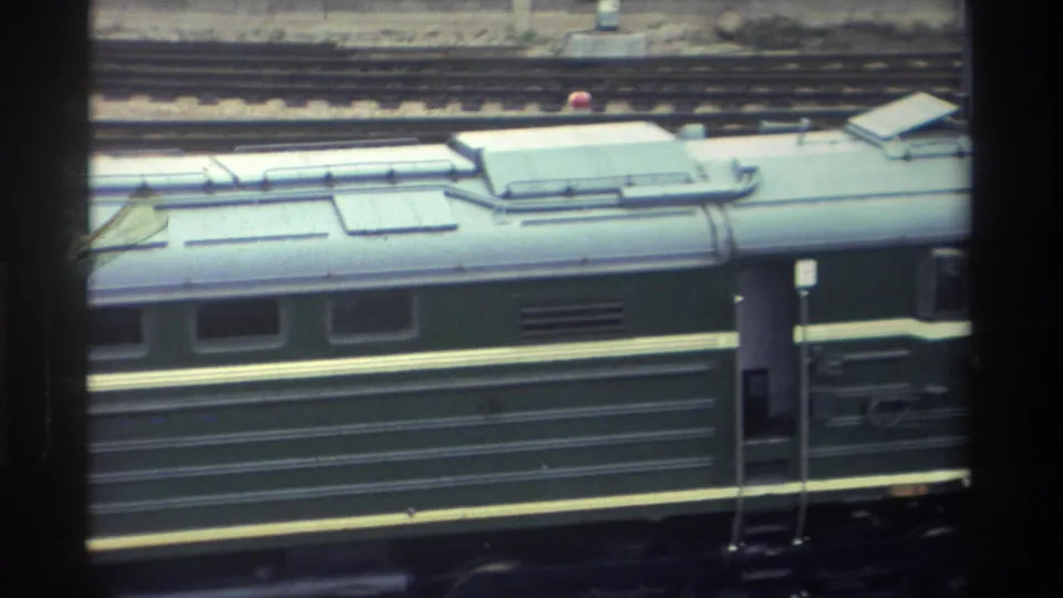 8mm film frame of a dark green passenger train car, possibly captured in Taiwan circa 1982 at the start of a tourist travel reel.