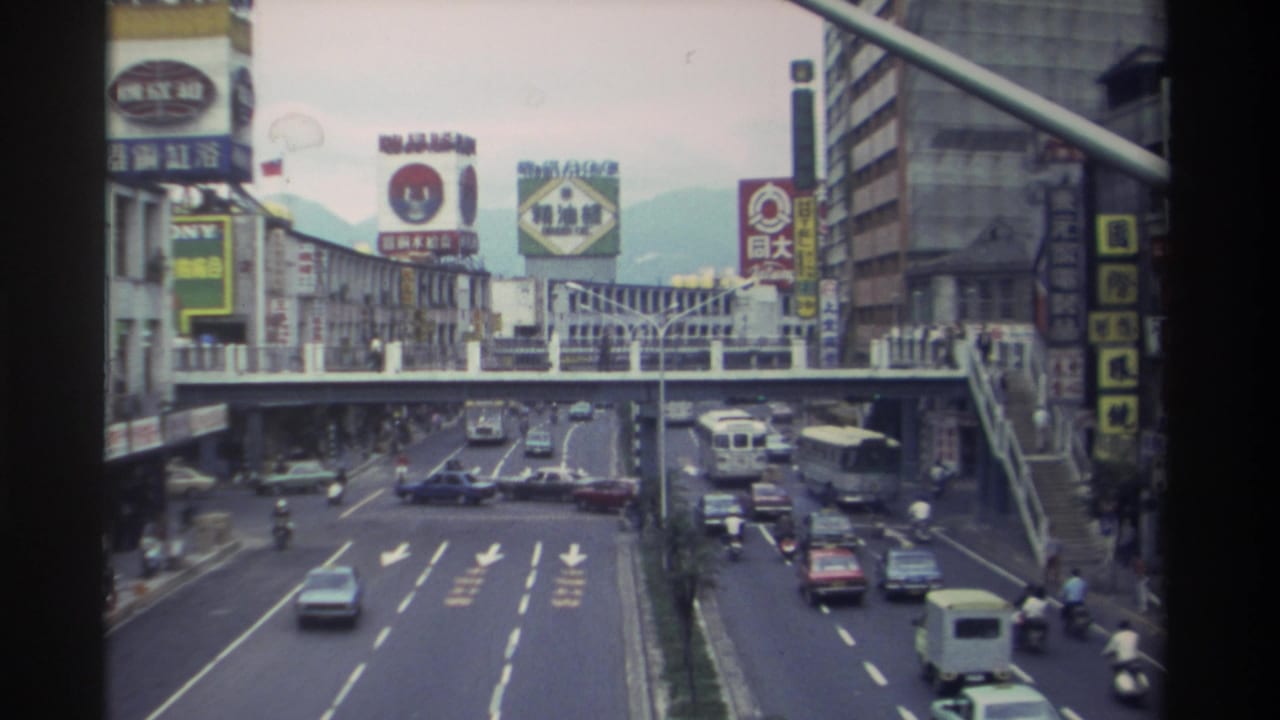 Elevated view of traffic flowing on a multi-lane road in Taiwan, circa 1982, showing 1980s-era cars, a white van, and Chinese-character billboard signage.