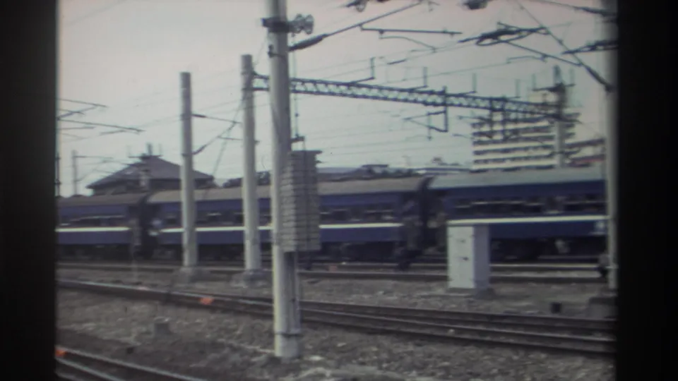 Taiwan rail yard circa 1982 with prominent catenary infrastructure; blue train coaches at lower frame edge, traditional-roofed structures visible mid-distance.