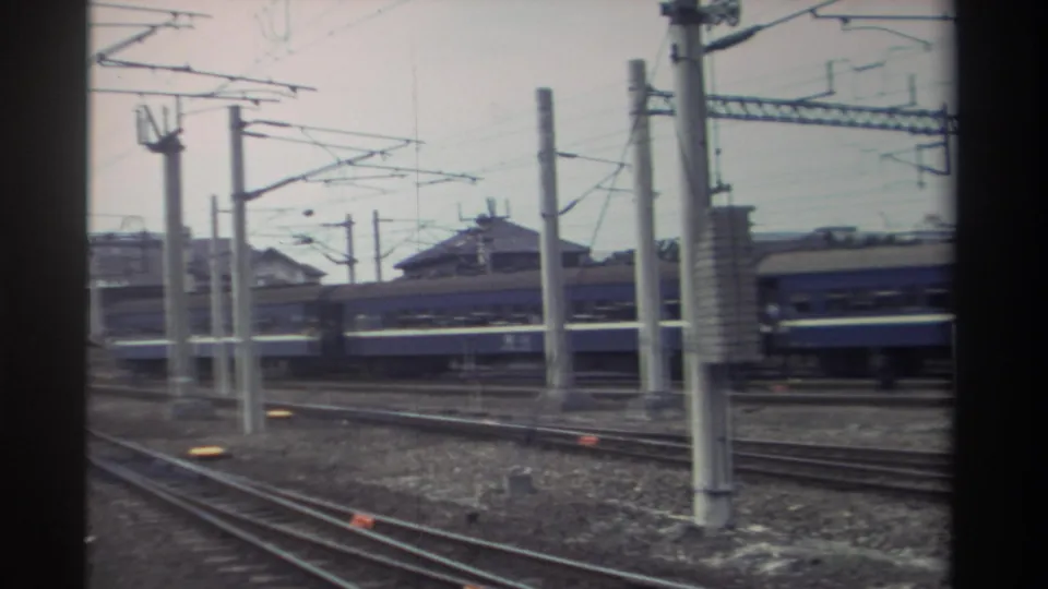 Taiwan urban rail yard, circa 1982, showing catenary infrastructure network and passing blue passenger train; low-rise structures with traditional rooflines visible.