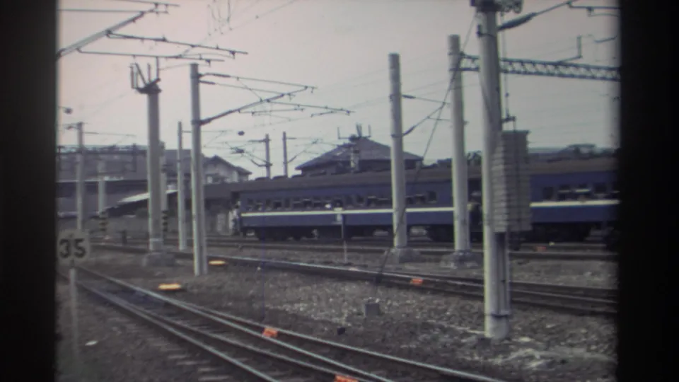 Elevated view of a Taiwanese rail yard, circa 1982; blue passenger rolling stock on adjacent tracks with catenary wires and a trackside '35' marker visible.