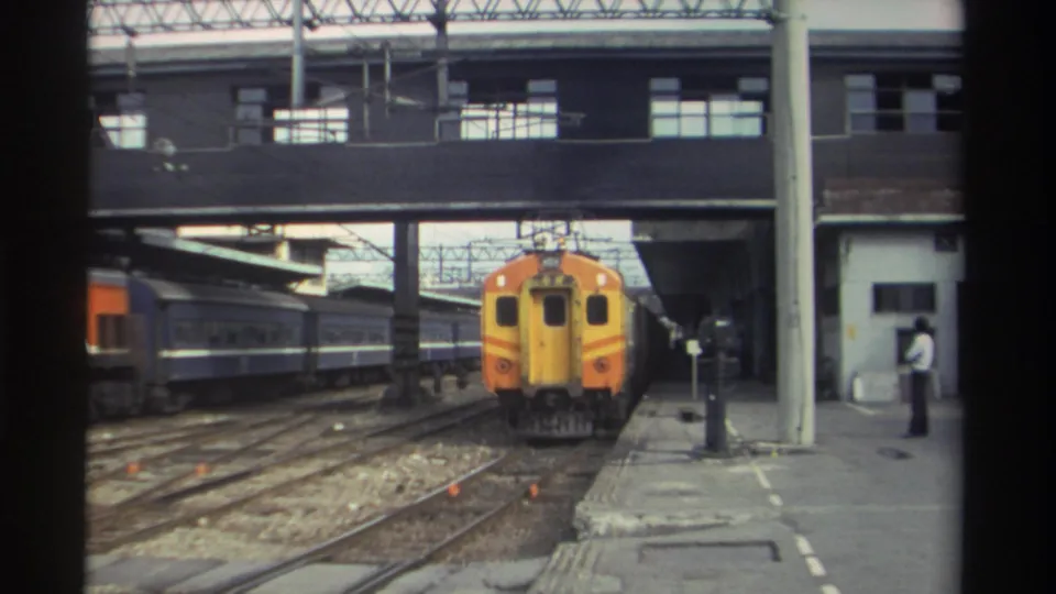 Taiwan railway station, circa 1982; orange and yellow locomotive at covered platform with a person in white visible at the platform edge.