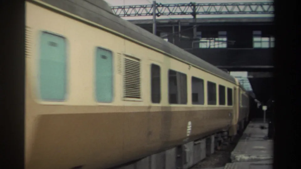 Cream-and-brown railway passenger coaches moving past the camera in 8mm footage, circa 1982 Taiwan, with turquoise door panels and station electrification gantry.